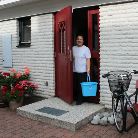 Medarbetare med hink i dörröppningen till ett hus med cykel bredvid
