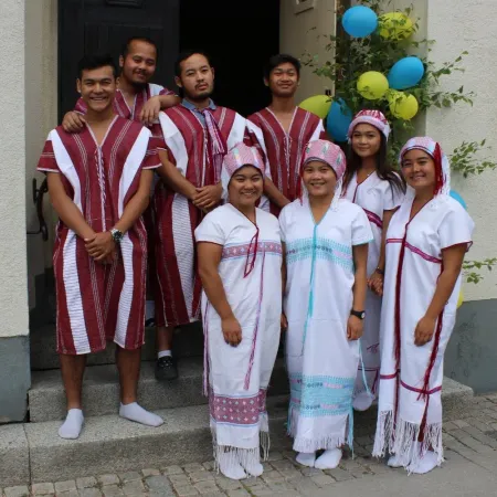 Grupp medarbetare i traditionella dräkter samlade vid en entré med ballonger